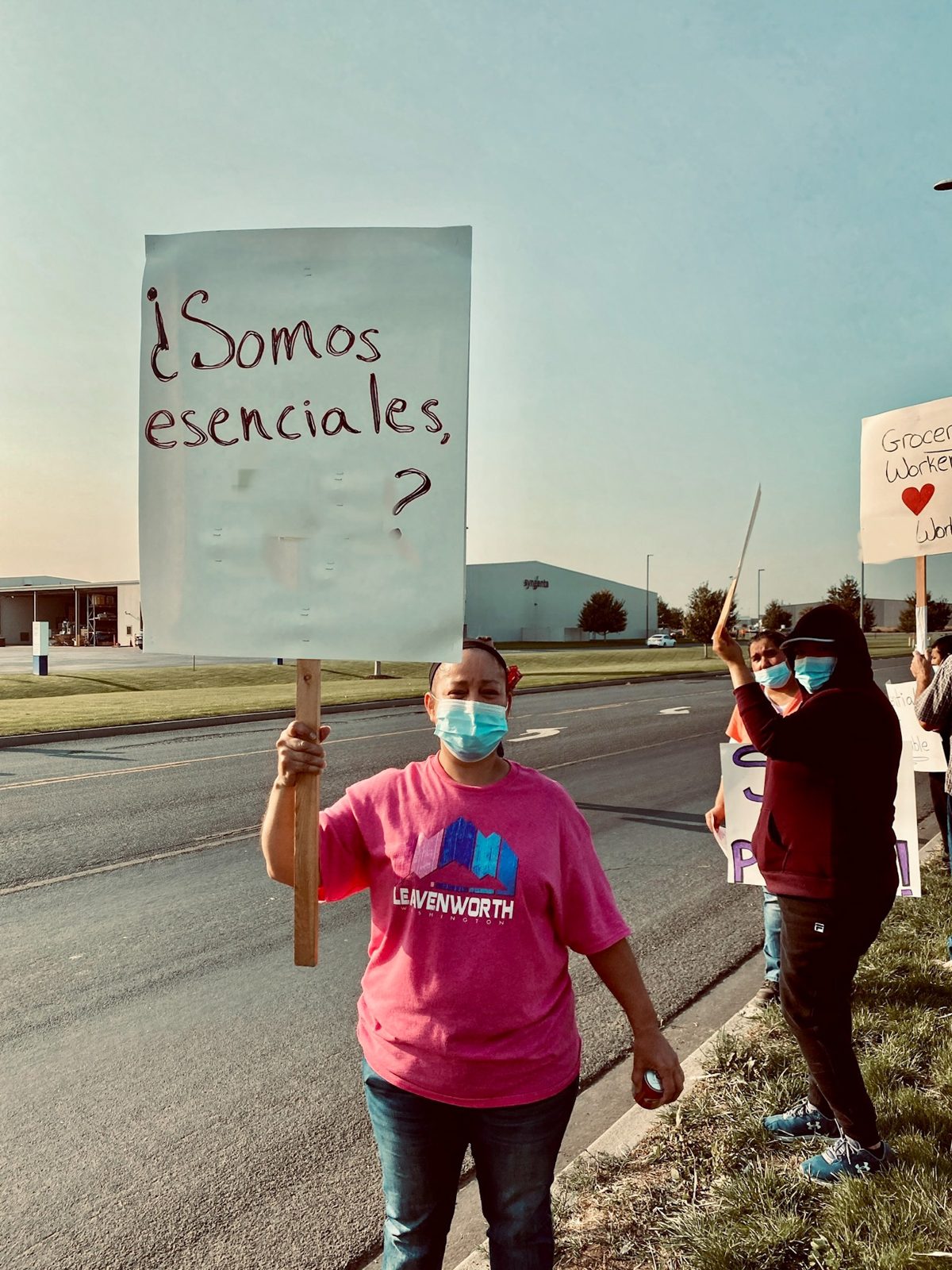 A worker holds a hand-lettered picket sign reading '¿Somos esenciales?'